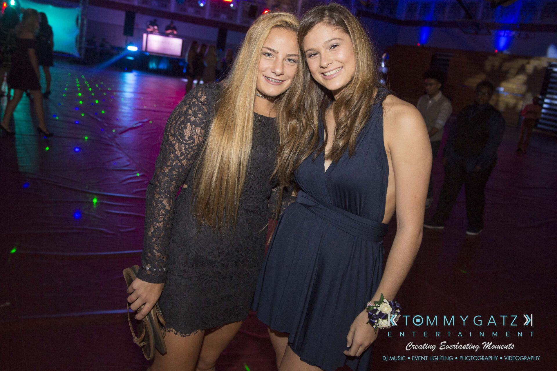 Broadneck-HC-FINAL-2017-BLOG-LoRes-WM-10 - TOMMY GATZ ENTERTAINMENT Two women in semi-formal attire smile at the camera in a dimly-lit event space with scattered colored lights.