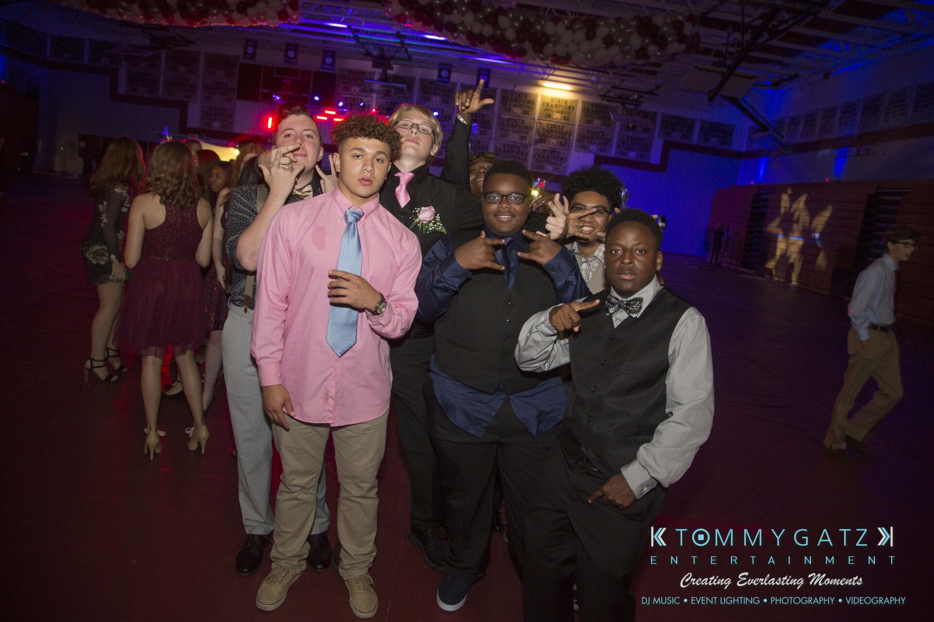 Broadneck-HC-FINAL-2017-BLOG-LoRes-WM-14 - TOMMY GATZ ENTERTAINMENT A group of young people pose for a photo in a dimly lit gymnasium during a celebration.