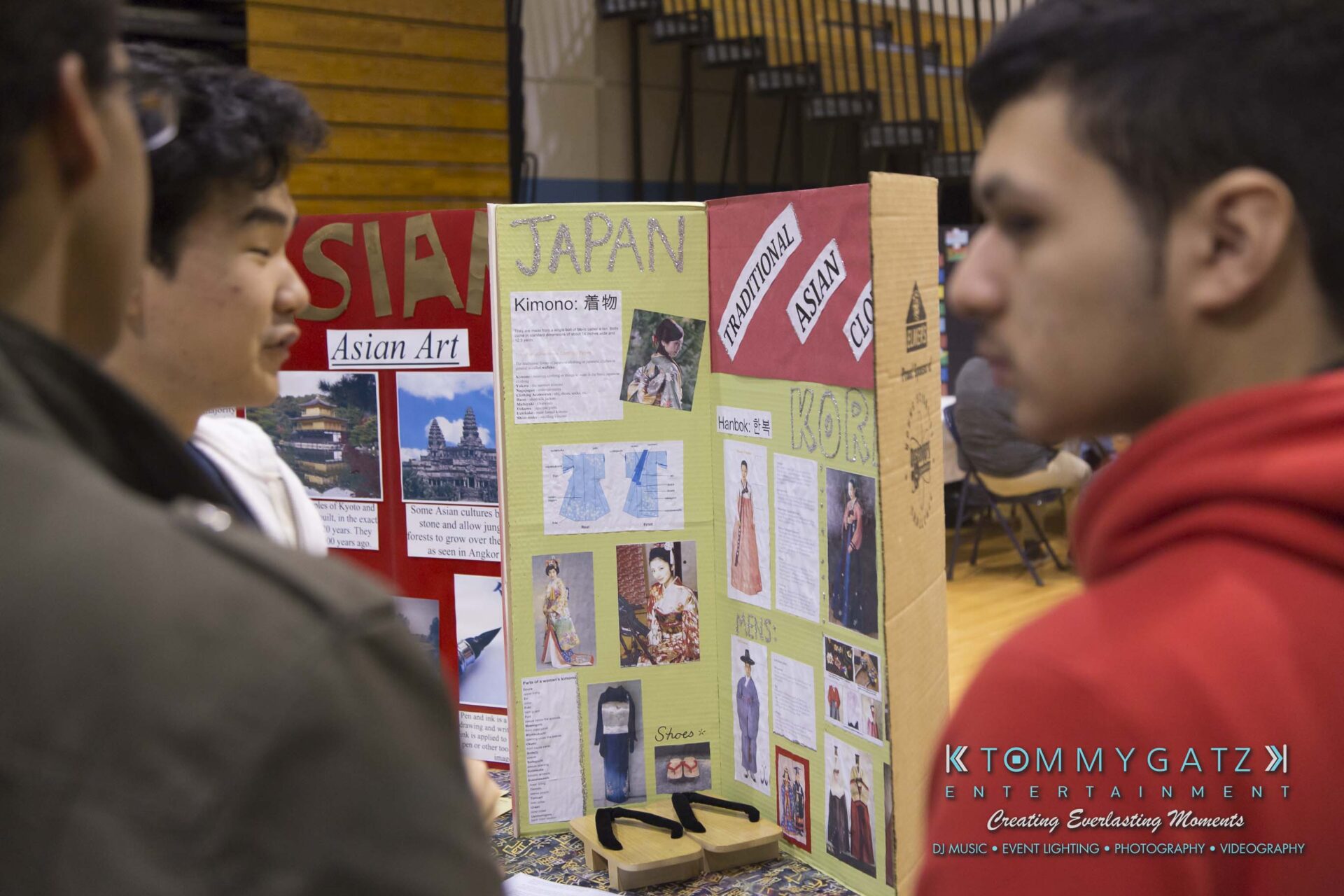 SR-Cultural-Day-2018-Low-Res-WM-26 - TOMMY GATZ ENTERTAINMENT Two people in conversation near a display board showcasing Japan, including images and text about kimonos and Asian art, in a gymnasium setting.