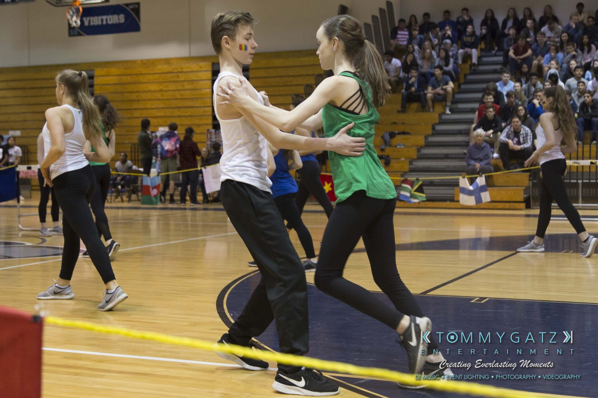 SR-Cultural-Day-2018-Low-Res-WM-34 - TOMMY GATZ ENTERTAINMENT Two young dancers practicing a routine in a gymnasium. Other dancers and spectators can be seen in the background.