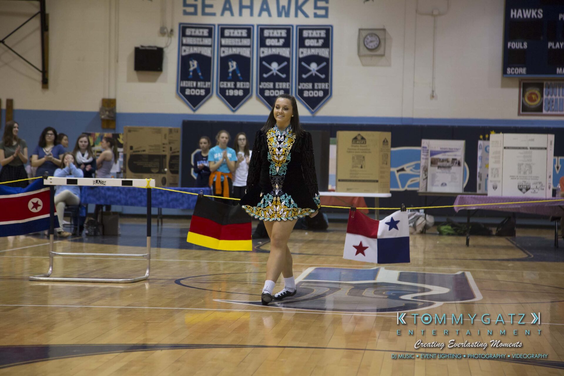 SR-Cultural-Day-2018-Low-Res-WM-40 - TOMMY GATZ ENTERTAINMENT A dancer in traditional Irish attire performs in a gymnasium decorated with international flags.