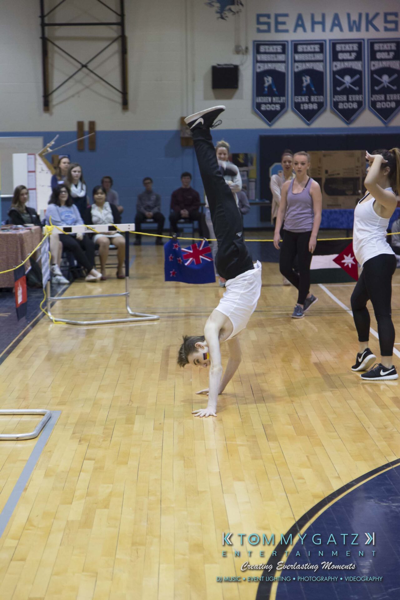 SR-Cultural-Day-2018-Low-Res-WM-46 - TOMMY GATZ ENTERTAINMENT A person performs a handstand on a gym floor during a gymnastics event, while others watch in the background.