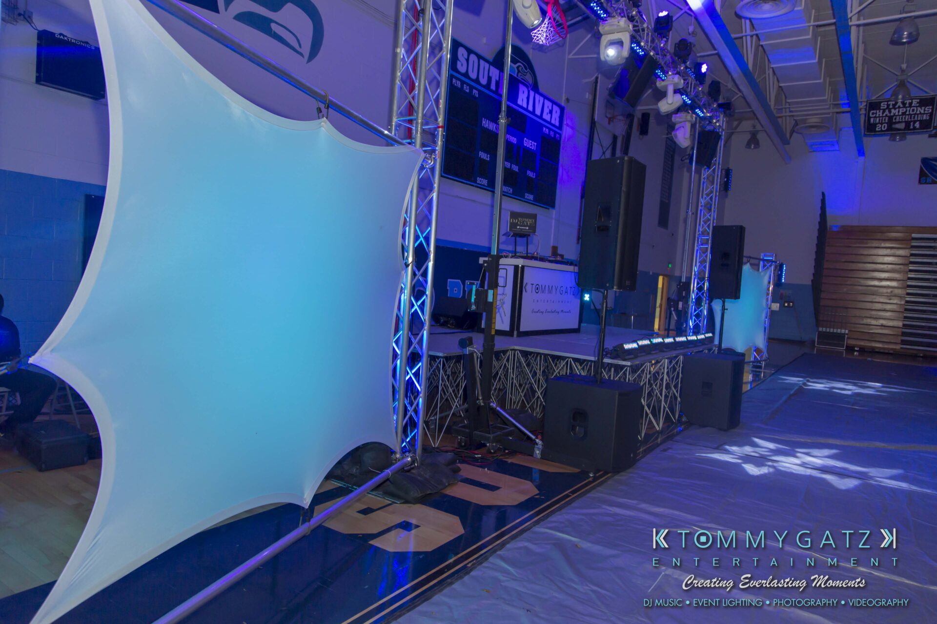 SR-HC-Dance-10717-BLOG-WM-2 1 - TOMMY GATZ ENTERTAINMENT Indoor event setup with large speakers, lighting equipment, and decorative fabric panels in a gym.