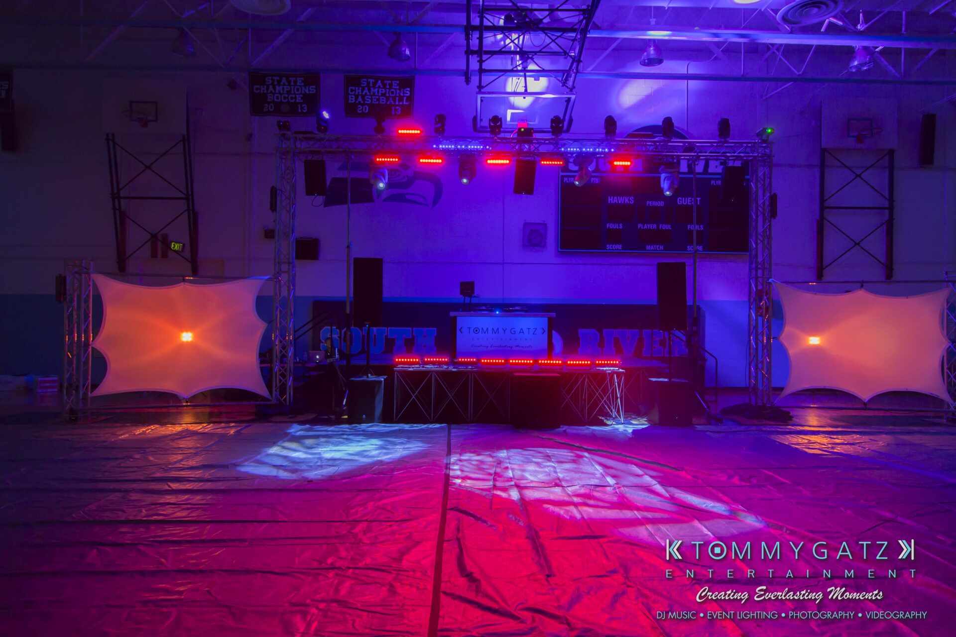 SR-HC-Dance-10717-BLOG-WM-3 - TOMMY GATZ ENTERTAINMENT A gymnasium set up as a dance floor with vibrant stage lights, speakers, and a DJ booth. The floor is partially covered with protective material.