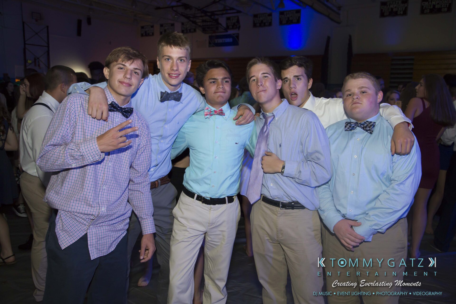 SR-HC-Dance-10717-BLOG-WM-37 - TOMMY GATZ ENTERTAINMENT A group of young men in dress shirts and bow ties pose together in a dimly lit indoor venue.