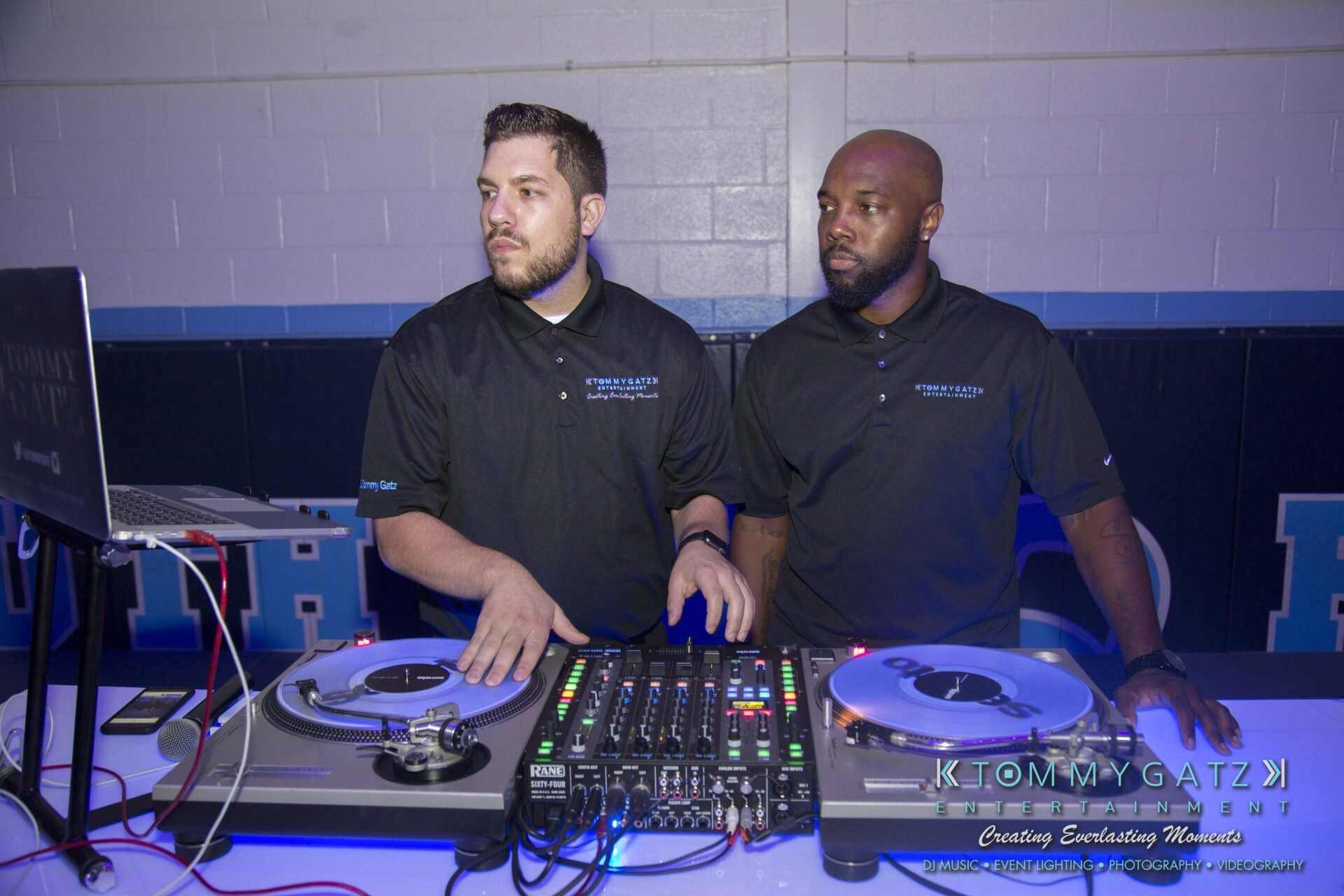 SR-HC-Dance-10717-BLOG-WM-4 - TOMMY GATZ ENTERTAINMENT Two DJs in black shirts operate turntables and a mixer on a table in a room with blue accents, focused on equipment and surroundings.