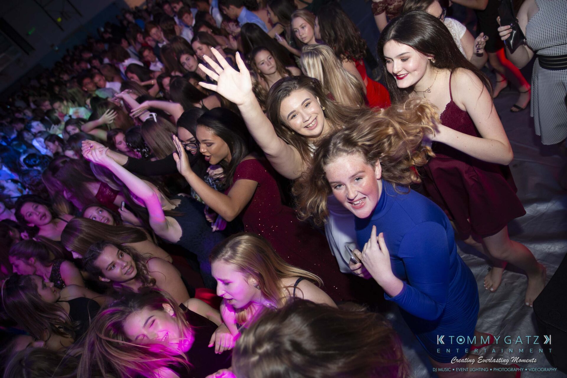 SR-Homecoming-102718-Carl-Low-Res-25 - TOMMY GATZ ENTERTAINMENT A group of people dancing and smiling at a crowded indoor event, with colorful lighting in the background.