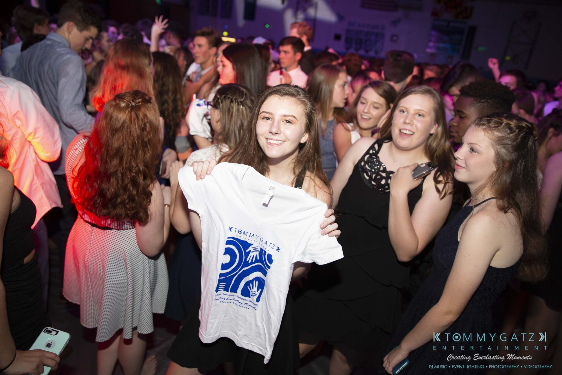 SR-Homecoming-102718-Carl-Low-Res-34 - TOMMY GATZ ENTERTAINMENT A young woman holds a T-shirt while surrounded by a group of dancing people at a crowded event.