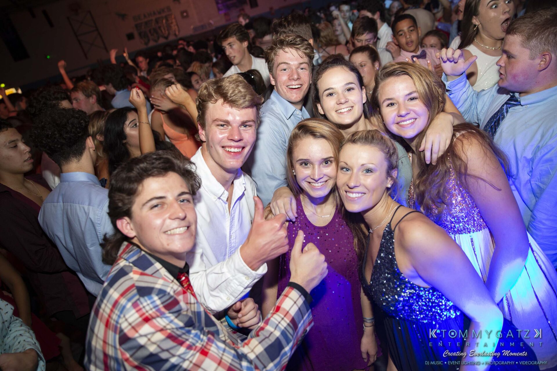 SR-Homecoming-102718-Carl-Low-Res-41 - TOMMY GATZ ENTERTAINMENT A group of young people smiling and posing at a lively indoor party with a large crowd in the background.