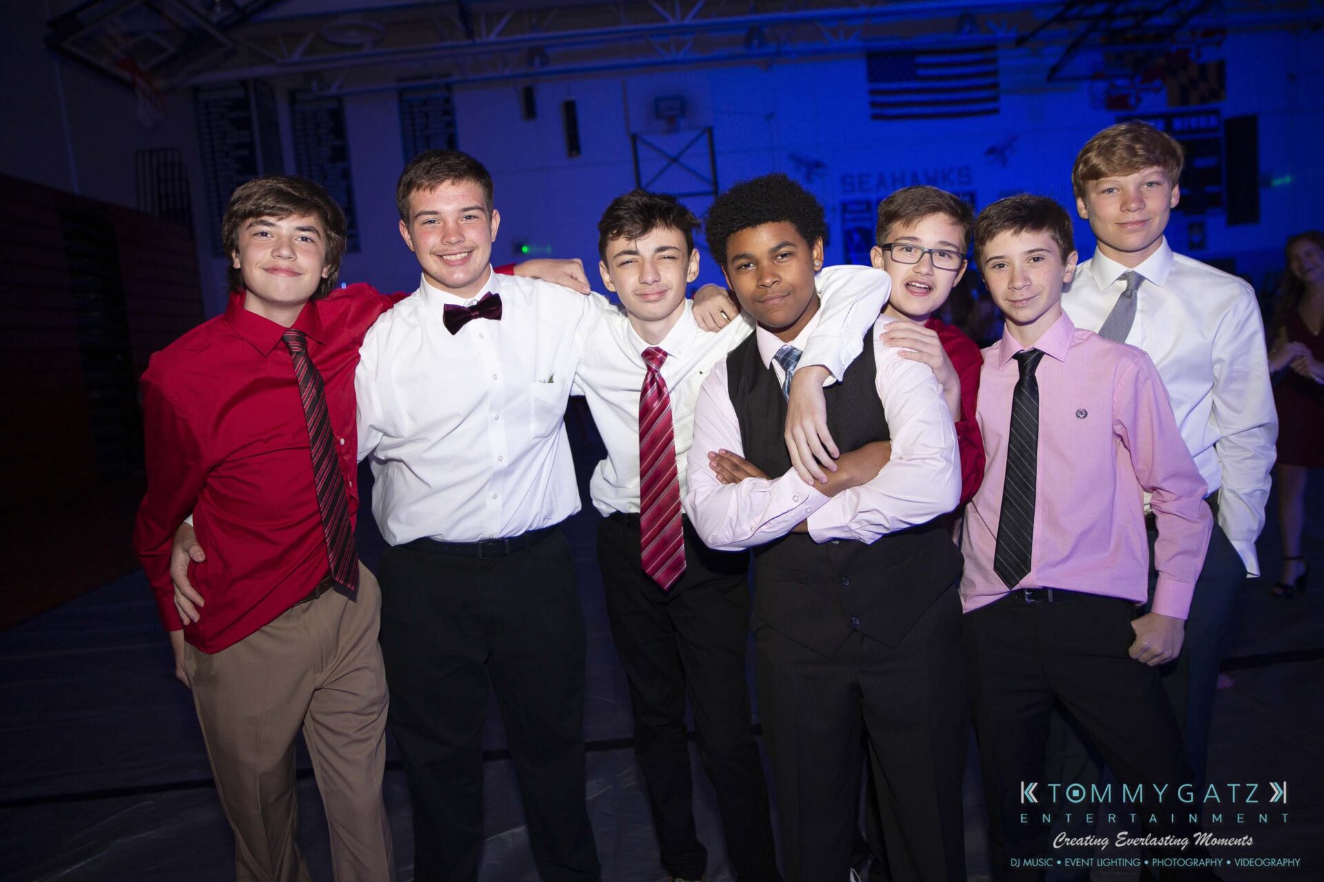 SR-Homecoming-102718-Carl-Low-Res-5 - TOMMY GATZ ENTERTAINMENT A group of seven young men dressed in formal attire pose together in a dimly lit room.