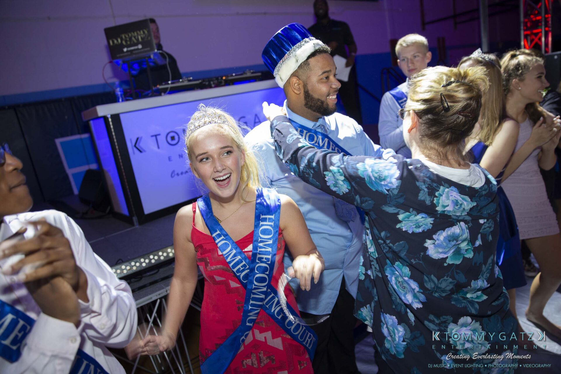 SR-Homecoming-102718-Carl-Low-Res-52 - TOMMY GATZ ENTERTAINMENT People dancing at a homecoming event. A young man wearing a crown smiles, while a young woman wearing a sash laughs. A DJ is in the background.