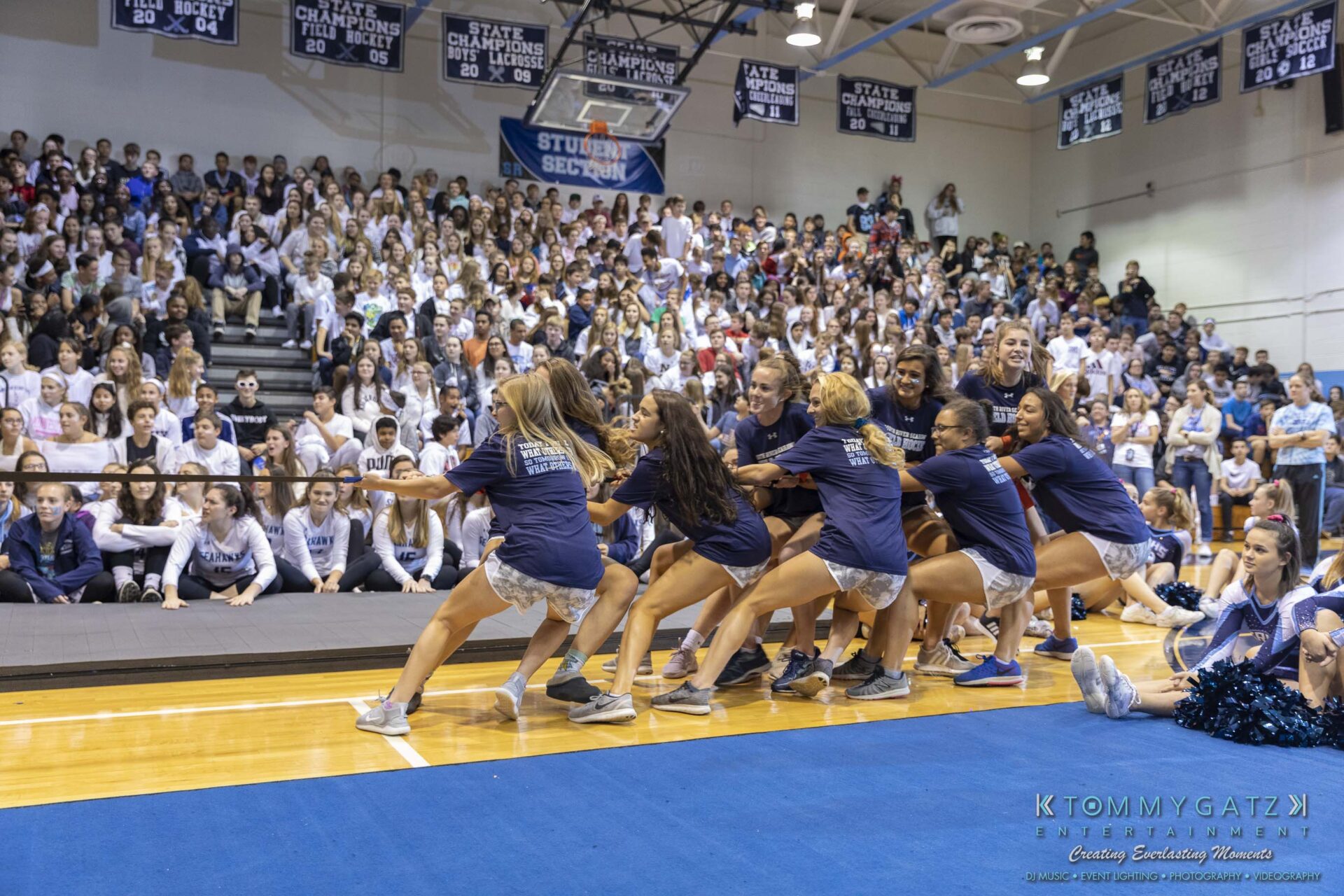 SR-Pep-Rally-102618-Carl-Low-Res-13 - TOMMY GATZ ENTERTAINMENT A group of people in matching shirts participate in a tug-of-war game inside a gymnasium, with a large audience watching from the bleachers.