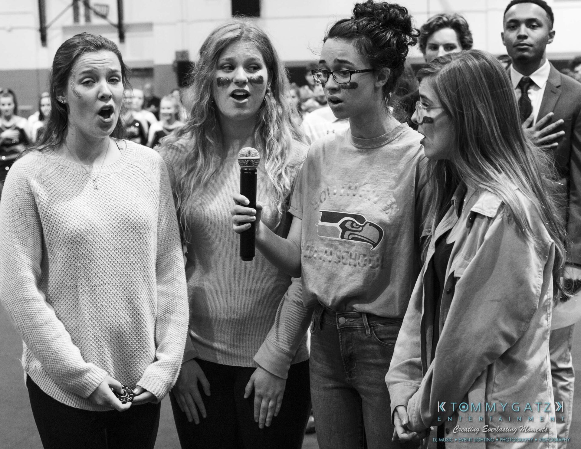 SR-Pep-Rally-102618-Carl-Low-Res-3 - TOMMY GATZ ENTERTAINMENT Four people sing into a microphone while a person in the background holds their hand over their heart.