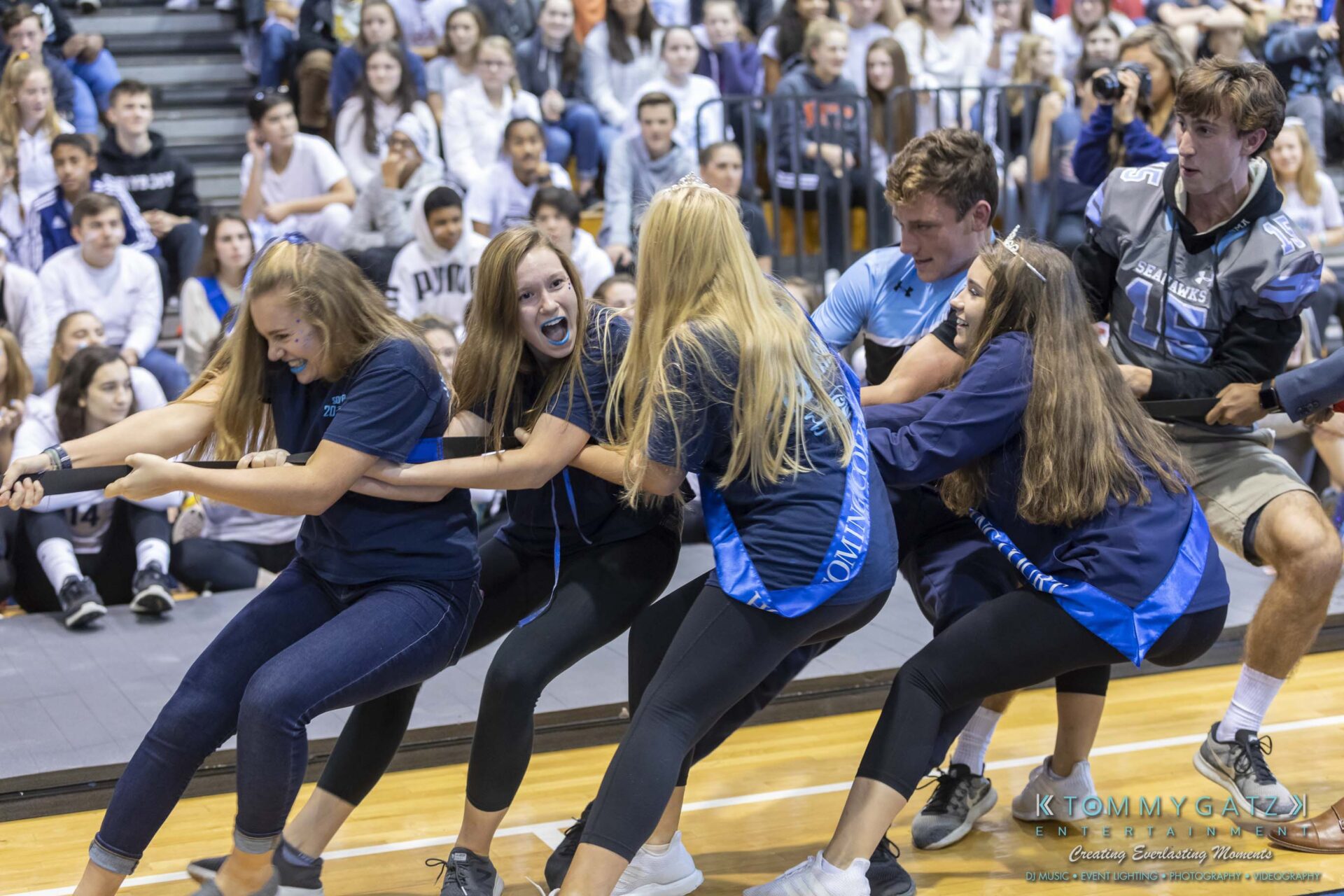 SR-Pep-Rally-102618-Carl-Low-Res-47 - TOMMY GATZ ENTERTAINMENT A group of students are playing tug-of-war in a gymnasium, with a large crowd seated in the background watching the event.