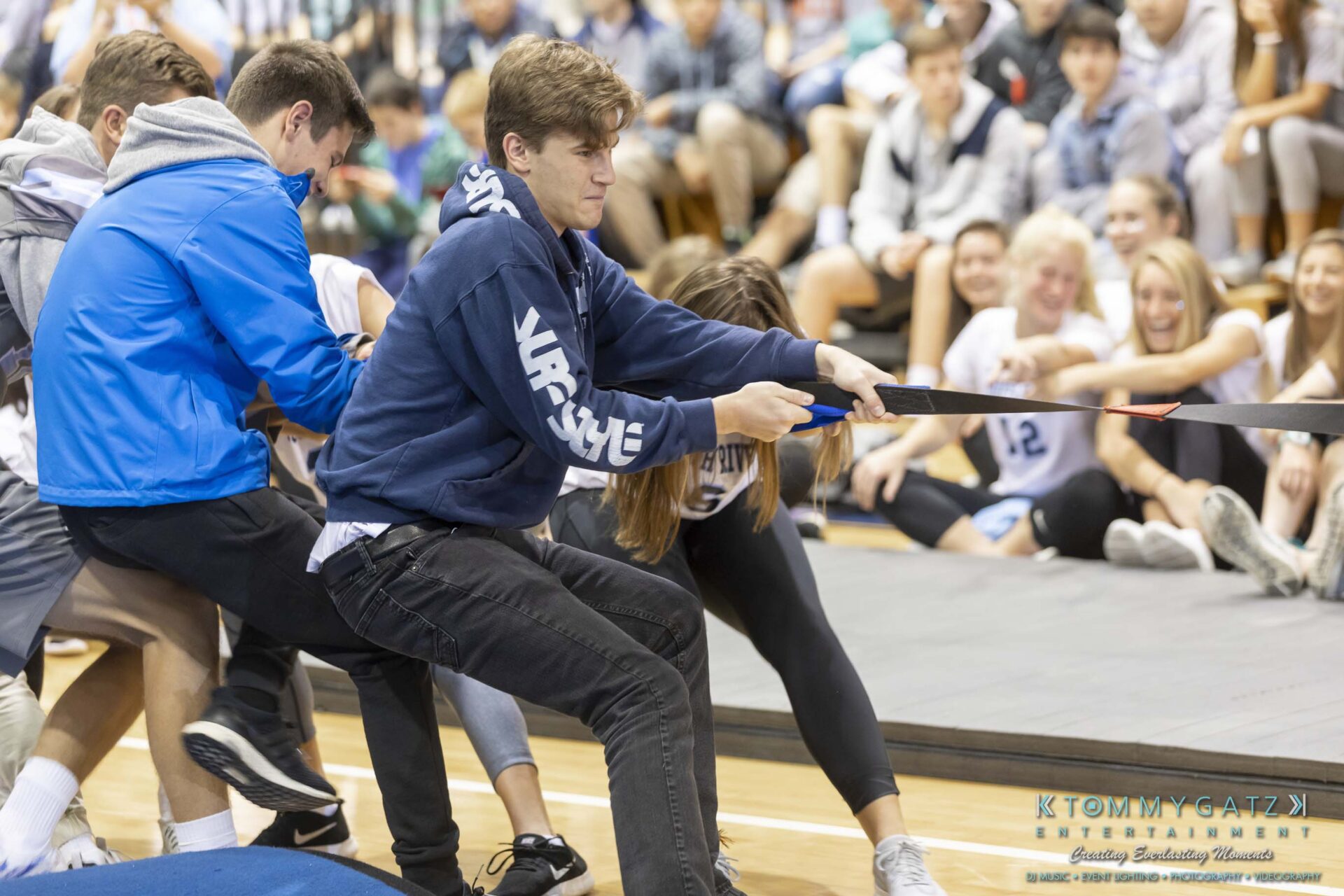 SR-Pep-Rally-102618-Carl-Low-Res-48 - TOMMY GATZ ENTERTAINMENT A group of people in a gymnasium engage in a tug-of-war, pulling a rope with determination. Spectators watch in the background.
