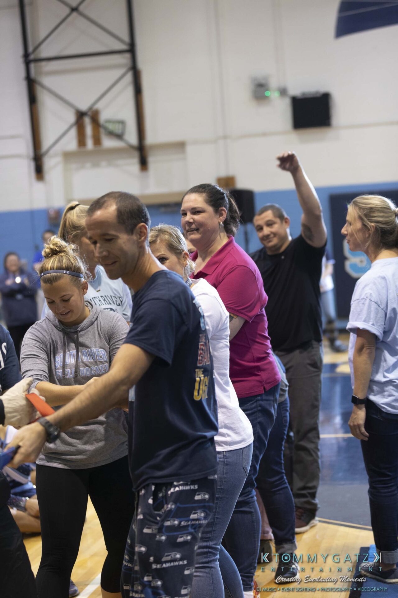 SR-Pep-Rally-102618-Carl-Low-Res-58 - TOMMY GATZ ENTERTAINMENT A group of people stand in a gym, engaging in an activity. One person gestures with their arm raised. The atmosphere appears lively and casual.