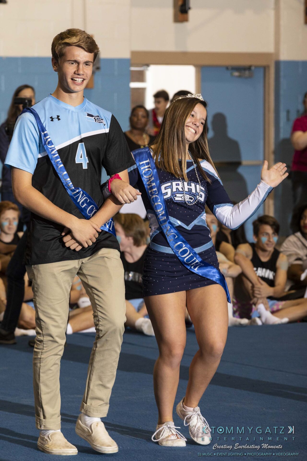 SR-Pep-Rally-102618-Carl-Low-Res-6 - TOMMY GATZ ENTERTAINMENT A young man and woman wearing sashes walk on a gym floor during an event. The woman waves to the crowd.