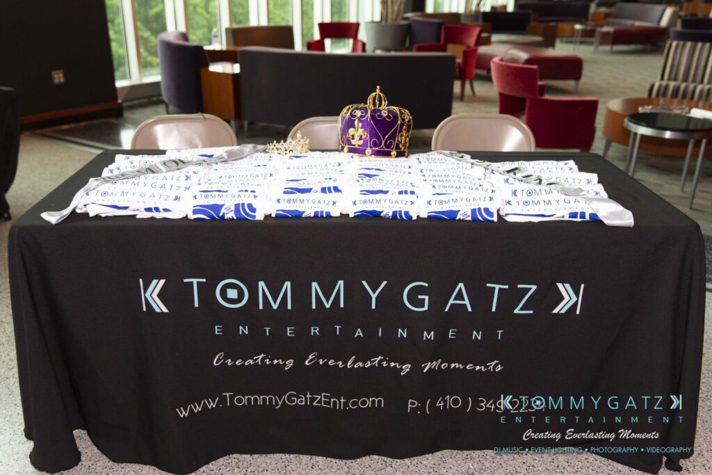 A table covered with a black Tommy Gatz Entertainment tablecloth, brochures, and a decorative crown.