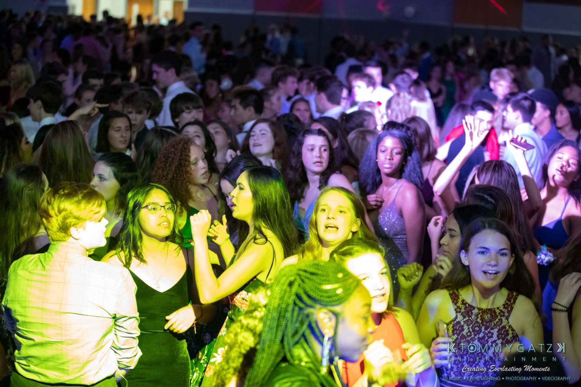092819-Broadneck-Homecoming-Low-Res-WM-37 - TOMMY GATZ ENTERTAINMENT A large group of people are dancing and socializing in a crowded indoor space with colorful lighting.