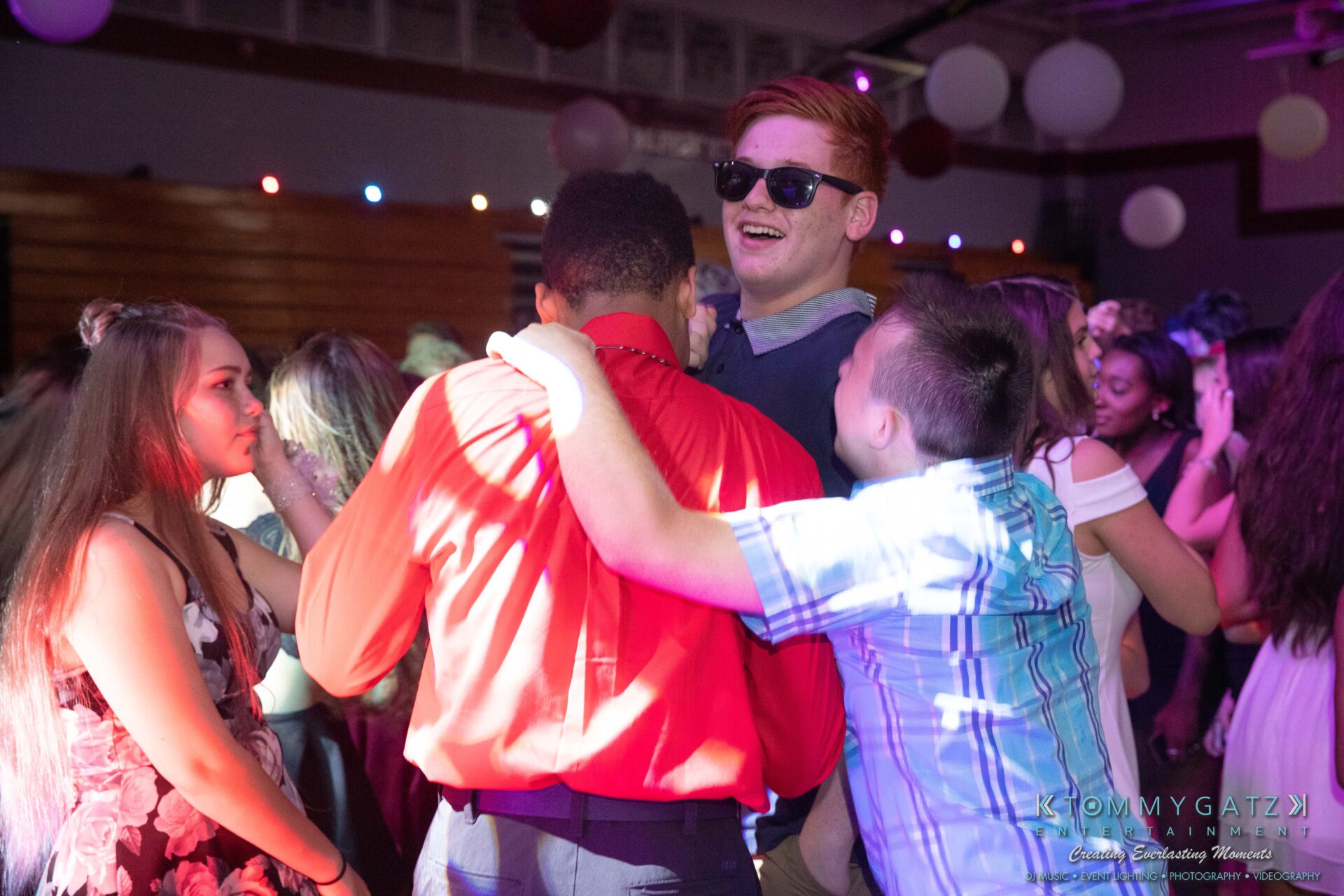 092819-Broadneck-Homecoming-Low-Res-WM-61 - TOMMY GATZ ENTERTAINMENT A group of people dancing at a lively indoor event, with balloons and lights in the background.