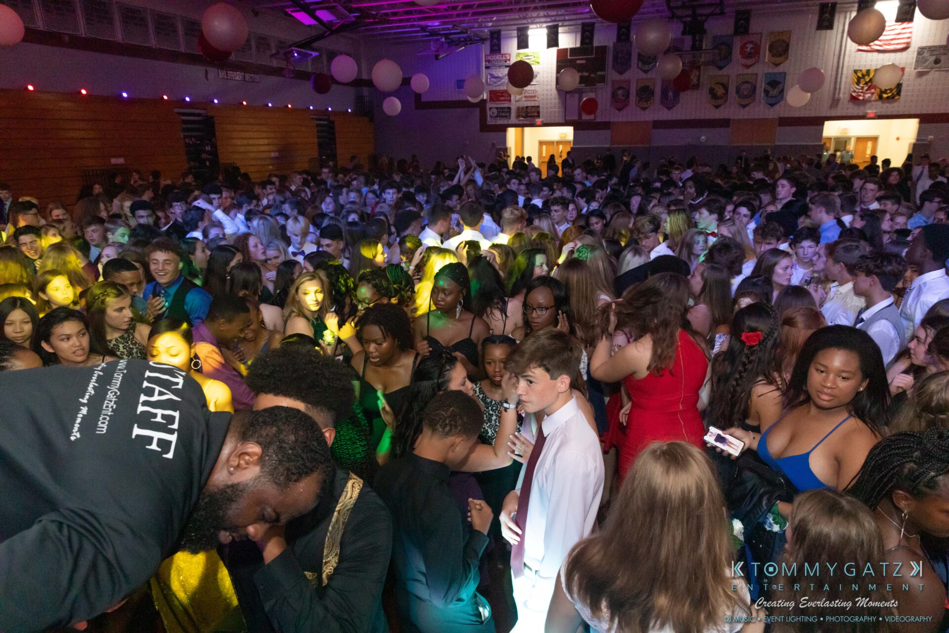 092819-Broadneck-Homecoming-Low-Res-WM-77 - TOMMY GATZ ENTERTAINMENT A large group of people dancing at an indoor event, with colorful lights and decorations.