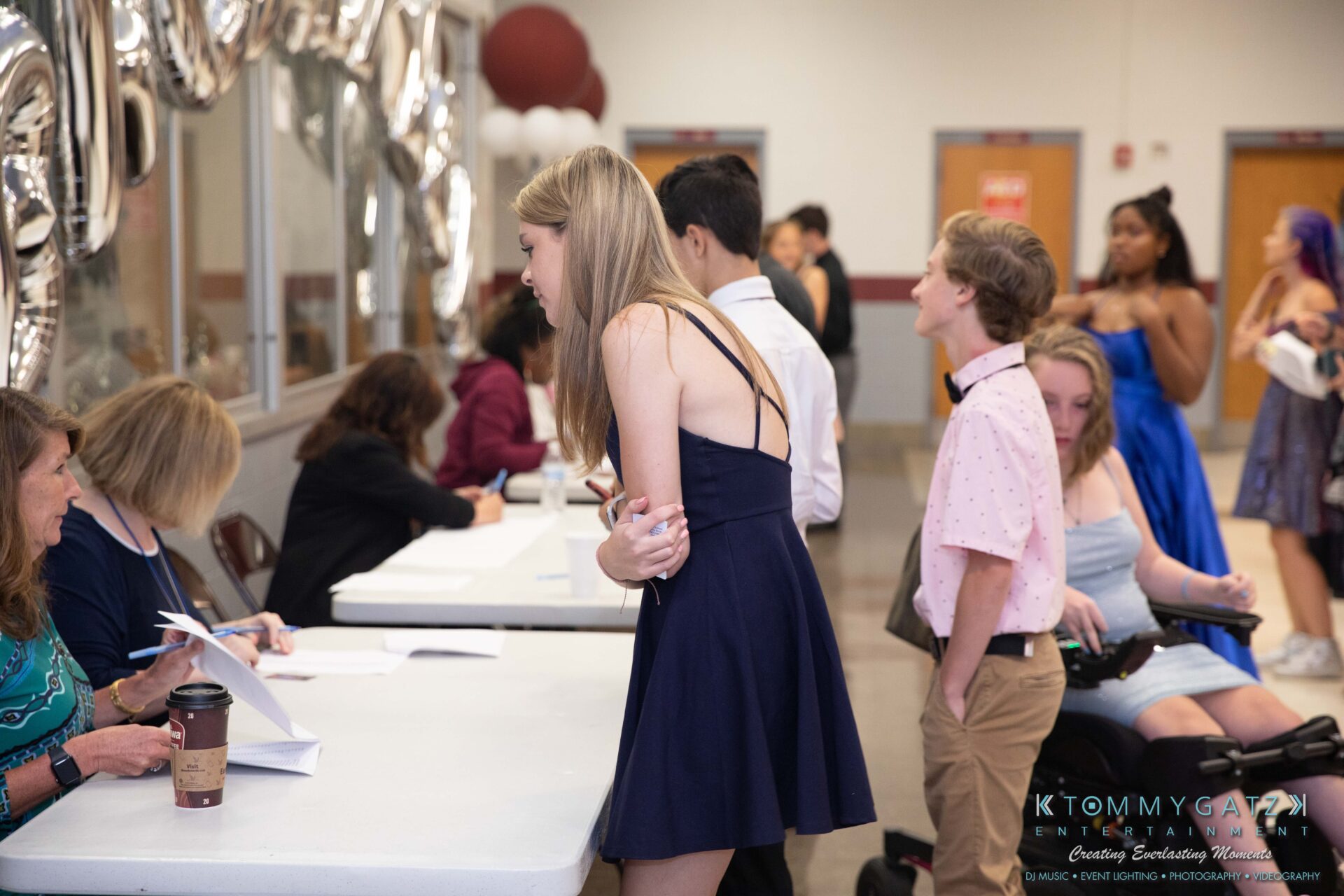 092819-Broadneck-Homecoming-Low-Res-WM-8 - TOMMY GATZ ENTERTAINMENT People check in at an event registration table in a community center. Balloons are visible in the background.