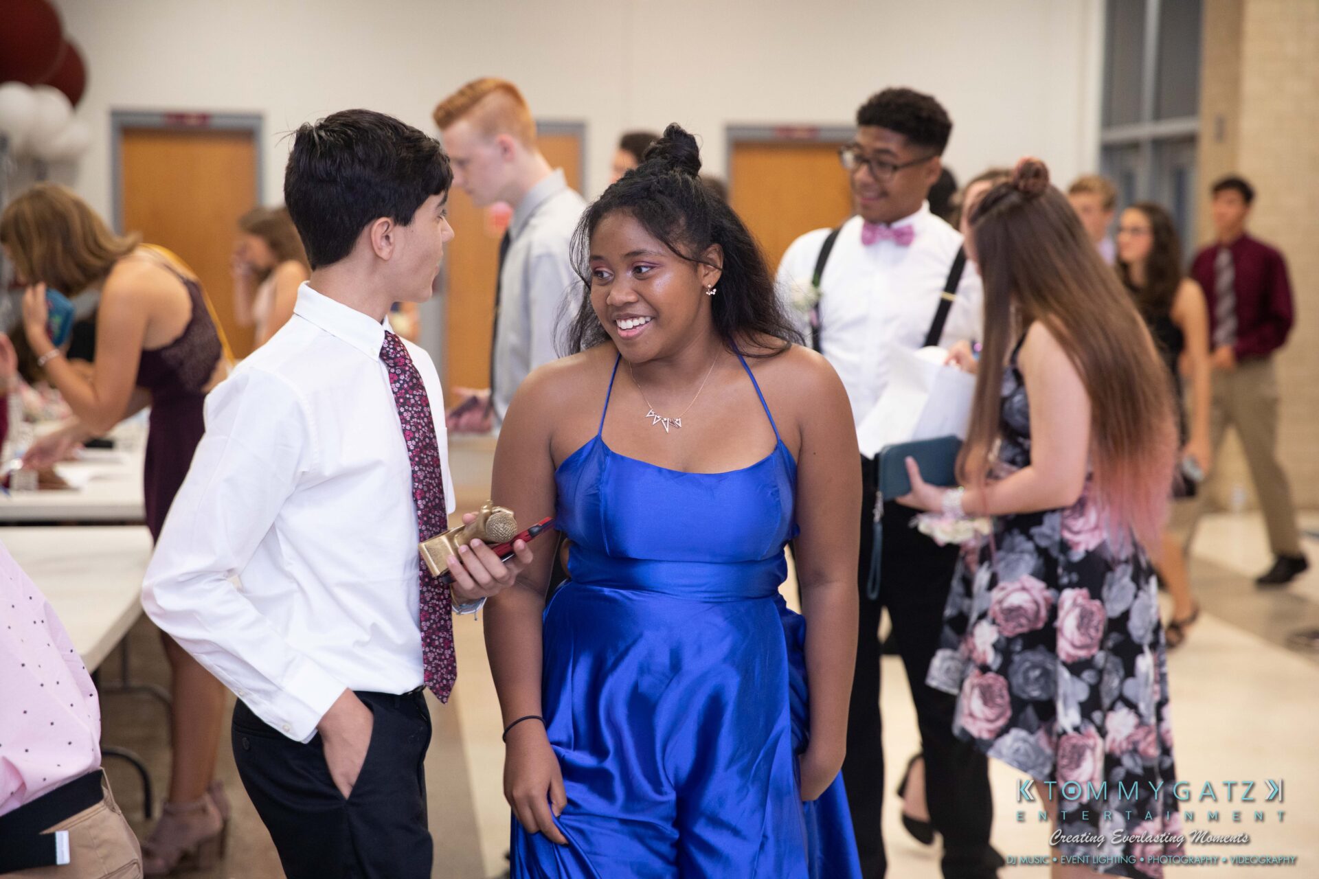 092819-Broadneck-Homecoming-Low-Res-WM-9-1 - TOMMY GATZ ENTERTAINMENT A group of young people in formal attire socializing at an indoor event. One person in a blue dress and others in suits and dresses are visible.