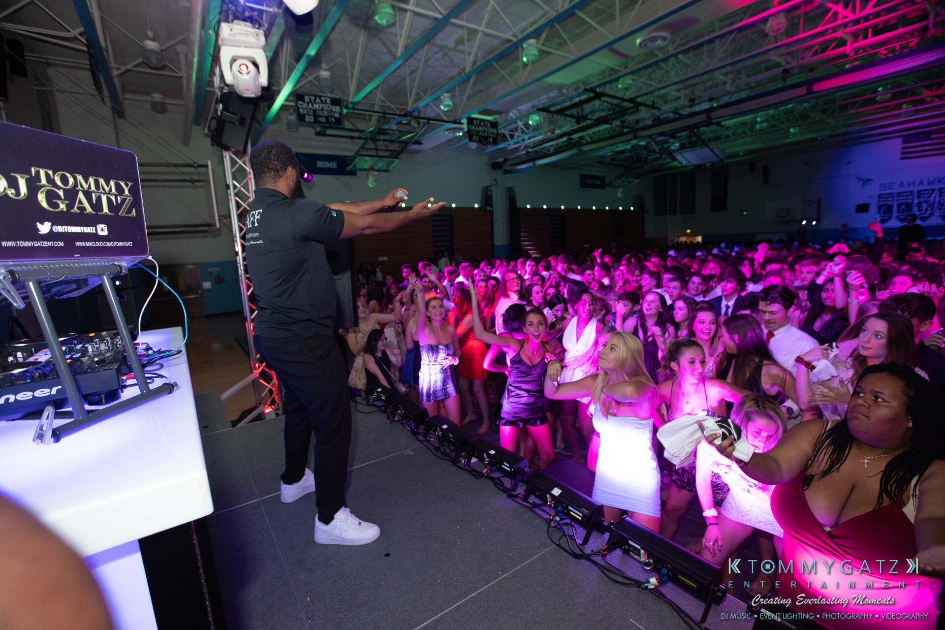 100519-South-River-HC-Dance-Low-Res-WM-37 - TOMMY GATZ ENTERTAINMENT DJ performing on stage in front of a crowd at an indoor event with colorful lighting.