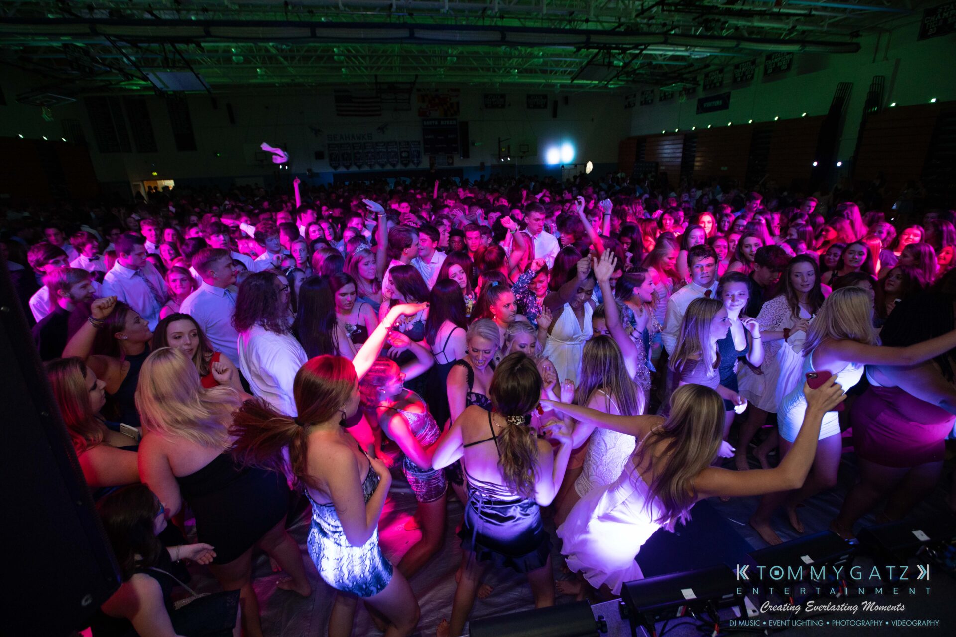 100519-South-River-HC-Dance-Low-Res-WM-40 - TOMMY GATZ ENTERTAINMENT A large crowd of people in formal attire dance under colorful lights at an indoor event.