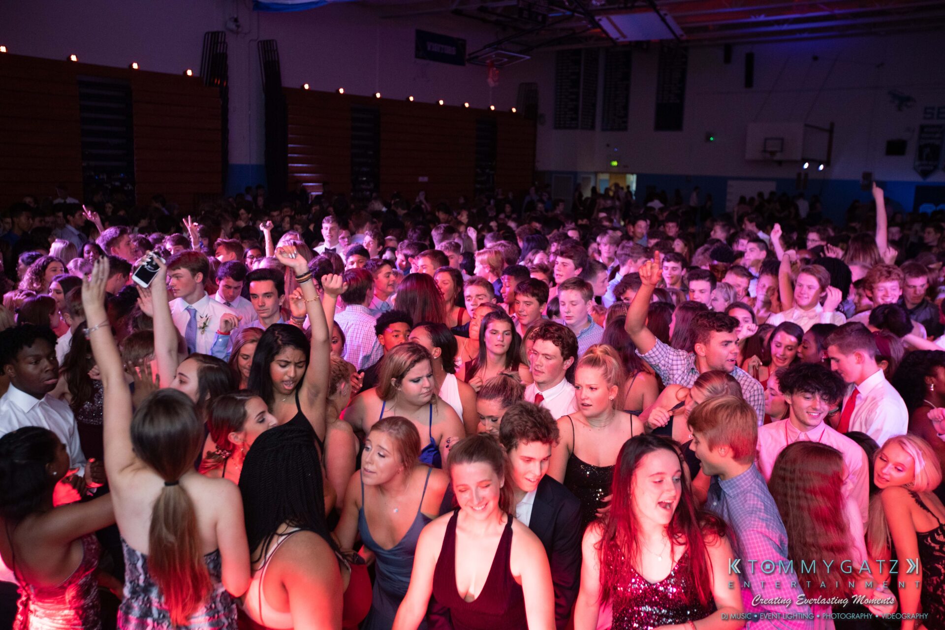 100519-South-River-HC-Dance-Low-Res-WM-56 - TOMMY GATZ ENTERTAINMENT A large group of people are dancing and socializing in a crowded indoor venue with colorful lighting.