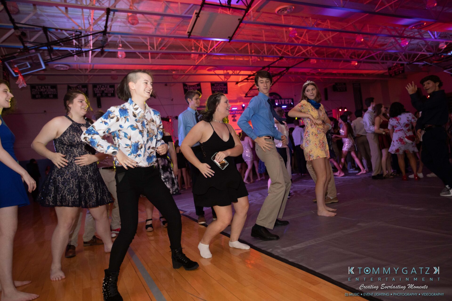 100519-South-River-HC-Dance-Low-Res-WM-66 - TOMMY GATZ ENTERTAINMENT People dancing energetically in a gymnasium with colorful lighting and a lively atmosphere.