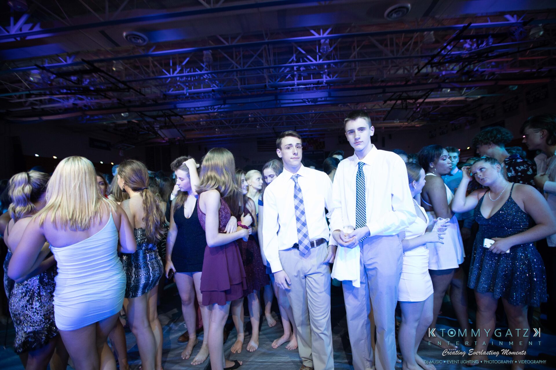 100519-South-River-HC-Dance-Low-Res-WM-89 - TOMMY GATZ ENTERTAINMENT A group of people, mostly young adults, dressed in formal attire at a party or dance event, under blue and purple lighting.