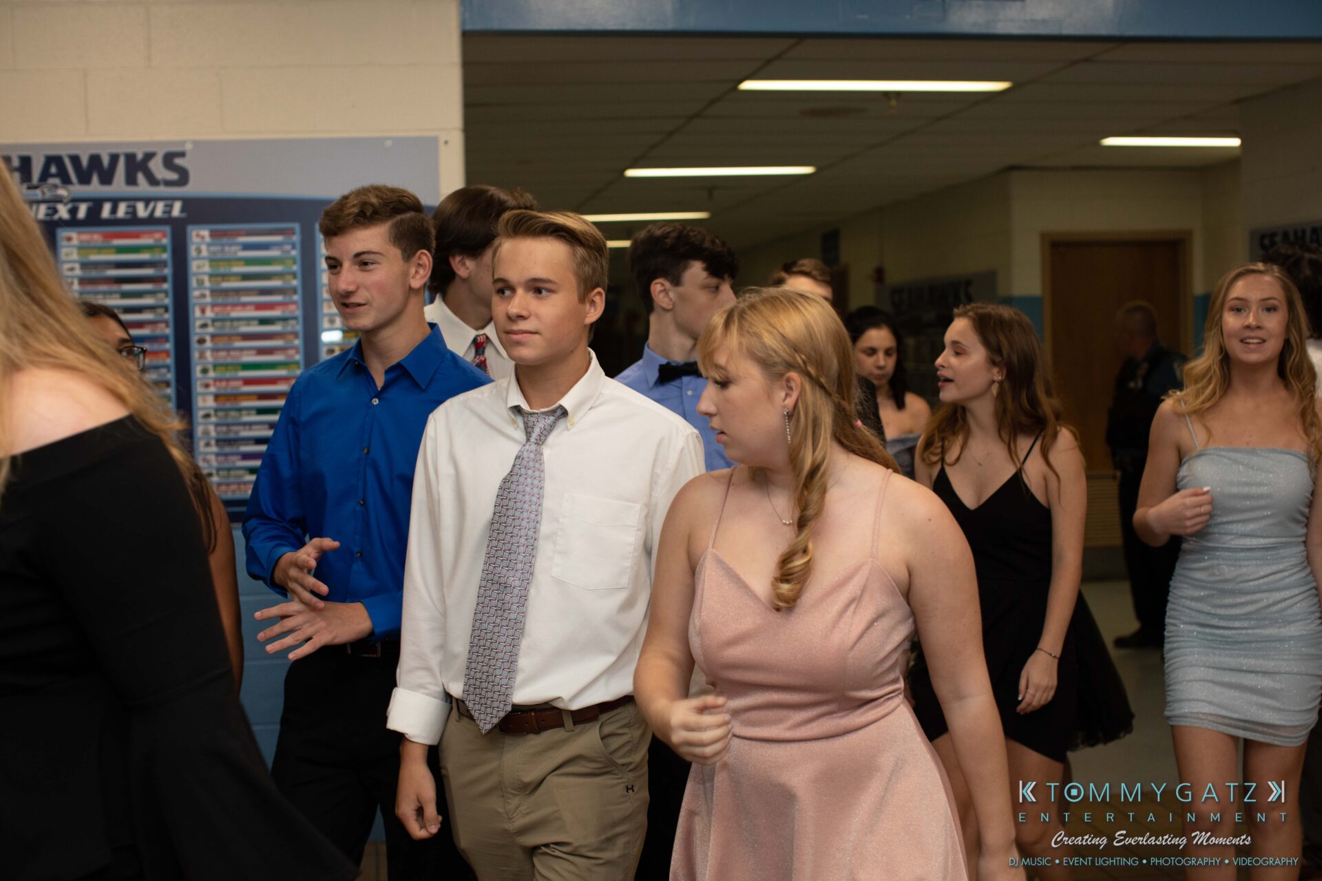 100519-South-River-HC-Dance-Low-Res-WM-9 - TOMMY GATZ ENTERTAINMENT Group of young people in semi-formal attire walking in a hallway, with some conversing and others looking ahead.