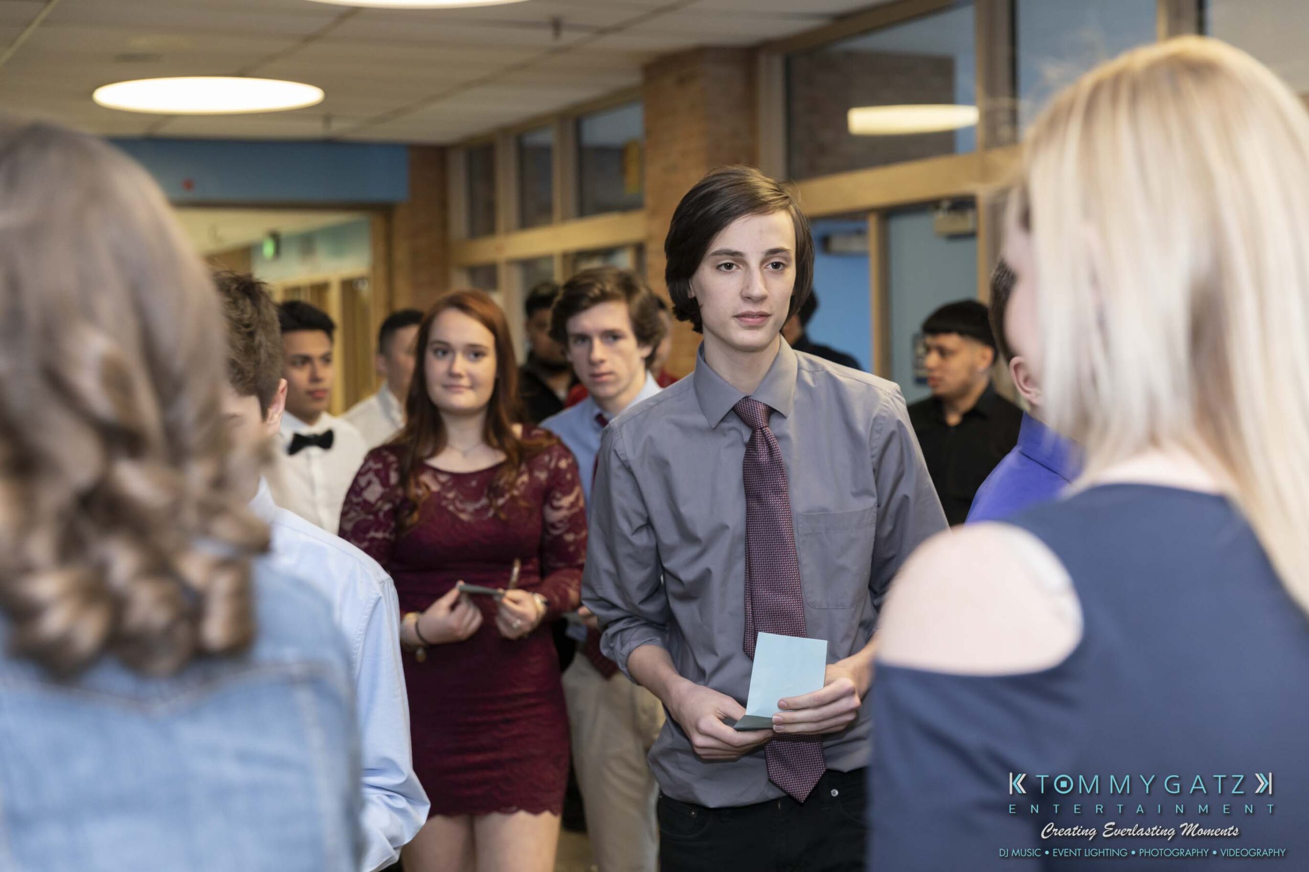 SR-Spring-Fling-032319-FINALS-Low-Res-WM-2 - TOMMY GATZ ENTERTAINMENT A group of people dressed in formal attire are walking down a hallway, holding papers. The scene appears to be at an event or gathering.