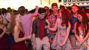 A group of young people dancing at a lively indoor event, wearing semi-formal attire.