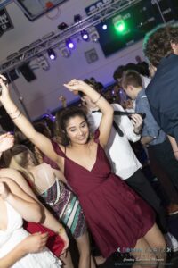 A group of people are dancing energetically in a dimly lit event space, with spotlights illuminating the scene.