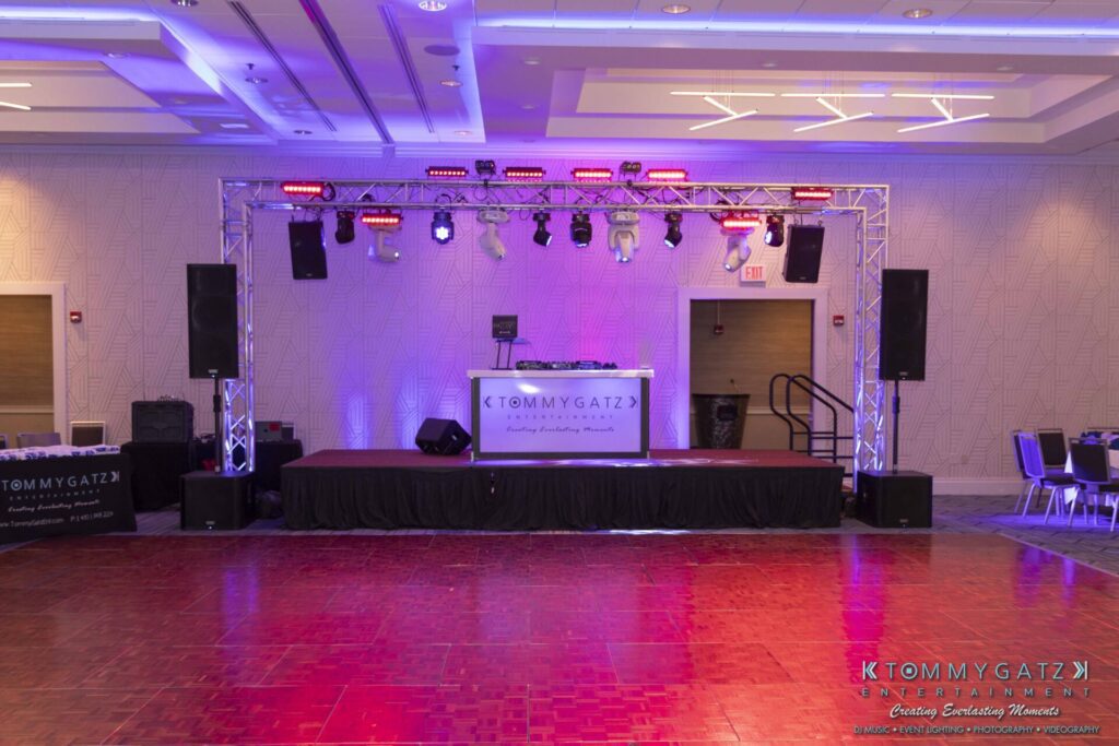 A DJ booth on a stage with speakers and lighting setup in a spacious event hall.