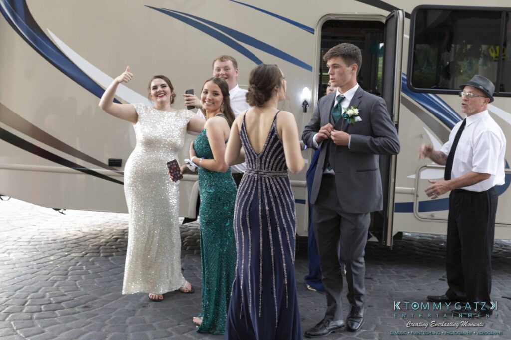 A group of people in formal attire stand outside a bus. One person is gesturing with a thumbs up.