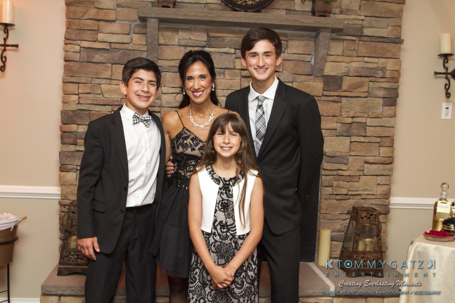 21 - TOMMY GATZ ENTERTAINMENT A woman stands in front of a fireplace with three children, all dressed formally.