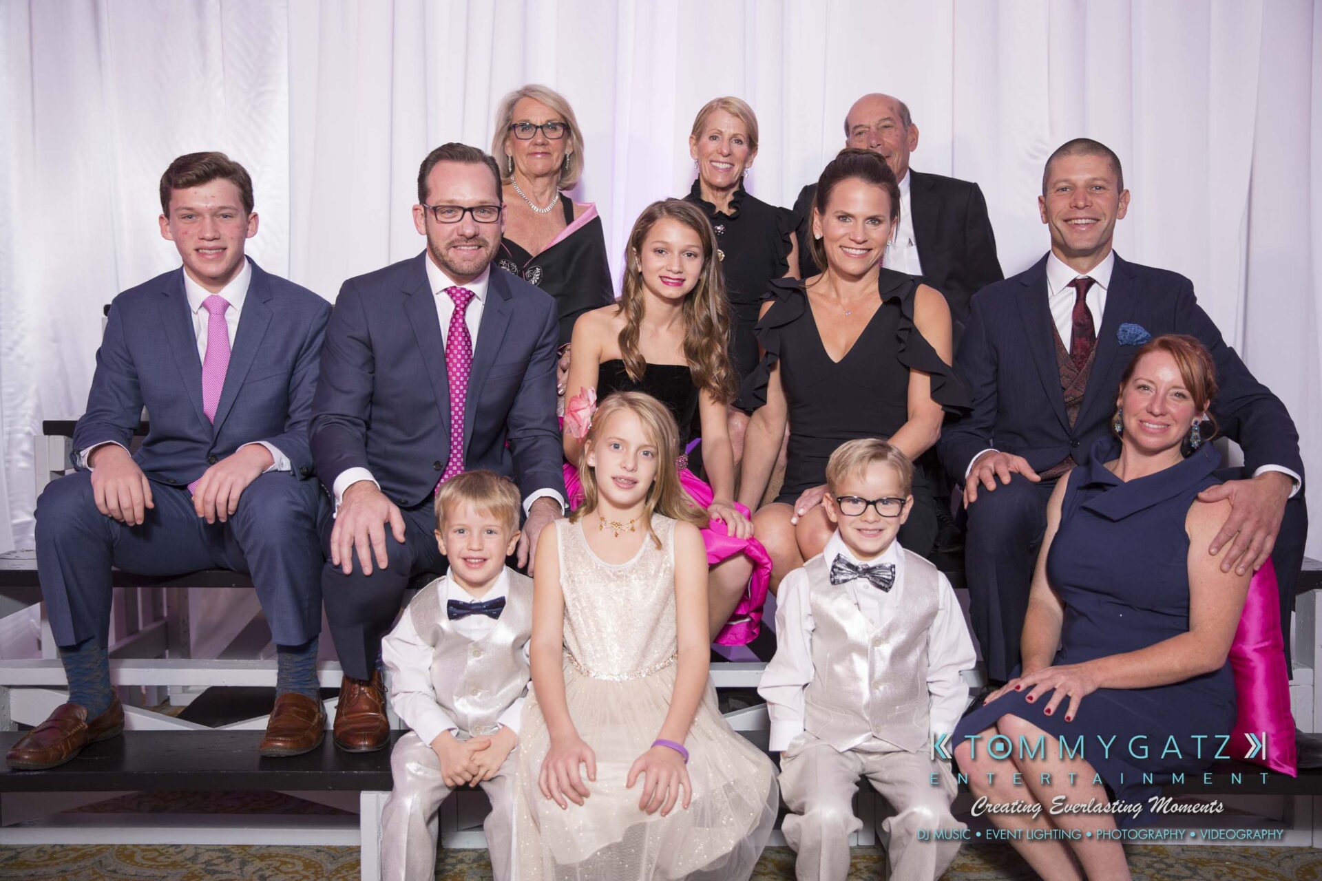 Dylans-Bat-Mitzvah-PORTRAITS-Low-Res-WM-22 - TOMMY GATZ ENTERTAINMENT A group of people in formal attire pose together for a photo. Some are seated, while others stand behind them.