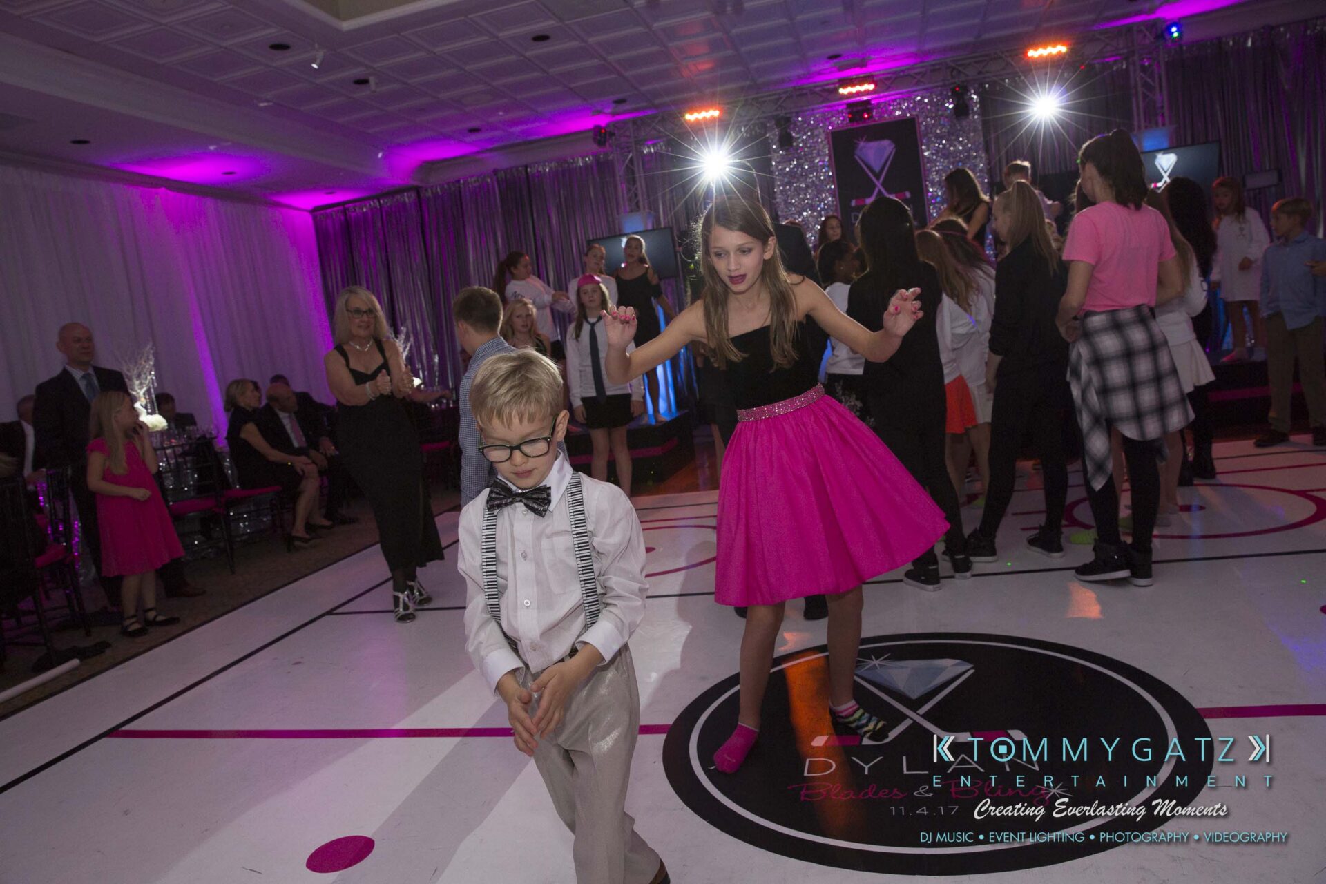 Dylans-Bat-Mitzvah-RECEPTION-Low-Res-WM-226 - TOMMY GATZ ENTERTAINMENT Children and adults dancing on a decorated dance floor at a party, with pink and purple lighting.