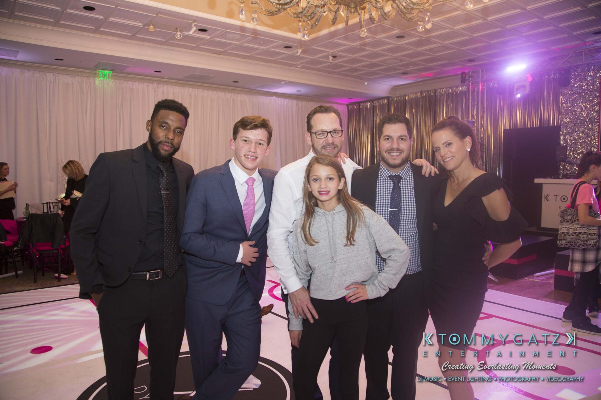 Dylans-Bat-Mitzvah-RECEPTION-Low-Res-WM-268 - TOMMY GATZ ENTERTAINMENT A group of six people, five adults and one child, posing together in a decorated indoor event space.