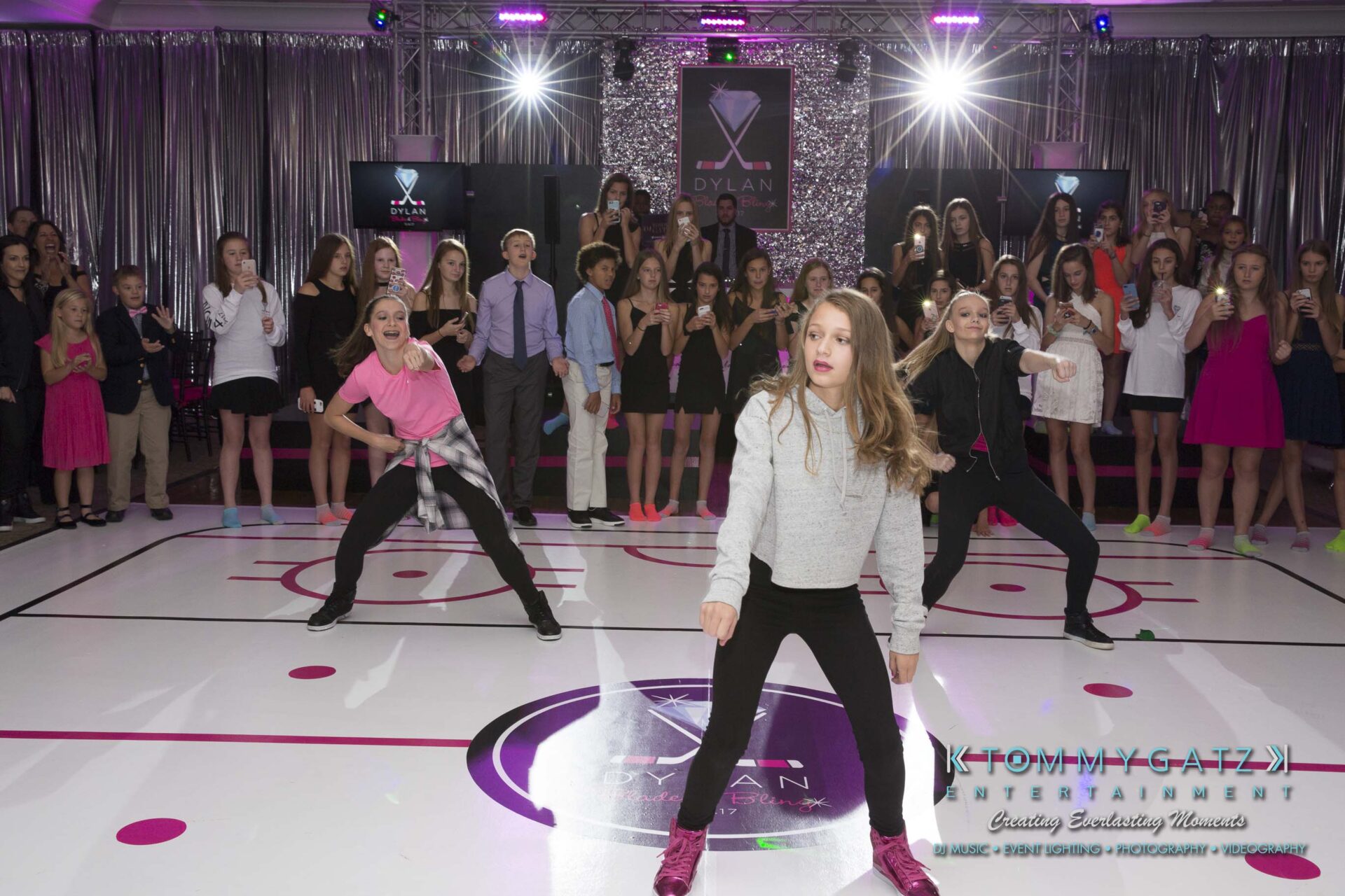 Dylans-Bat-Mitzvah-RECEPTION-Low-Res-WM-37 - TOMMY GATZ ENTERTAINMENT A group of young dancers performs energetically on a stage in front of an audience, under bright lights.