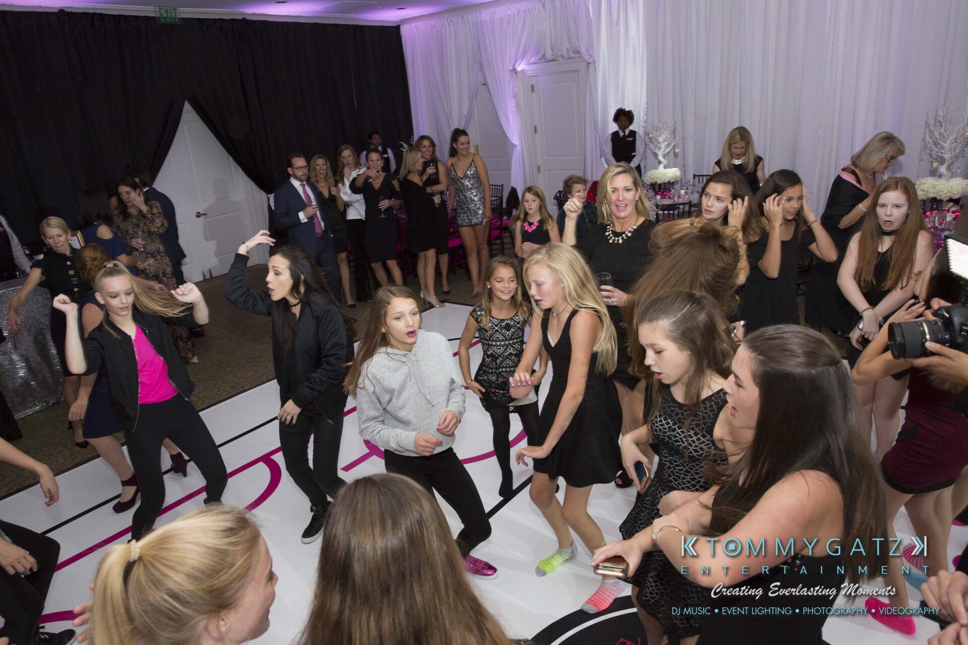 Dylans-Bat-Mitzvah-RECEPTION-Low-Res-WM-72 - TOMMY GATZ ENTERTAINMENT A group of people, mostly women and girls, dancing energetically at a party in a decorated venue.
