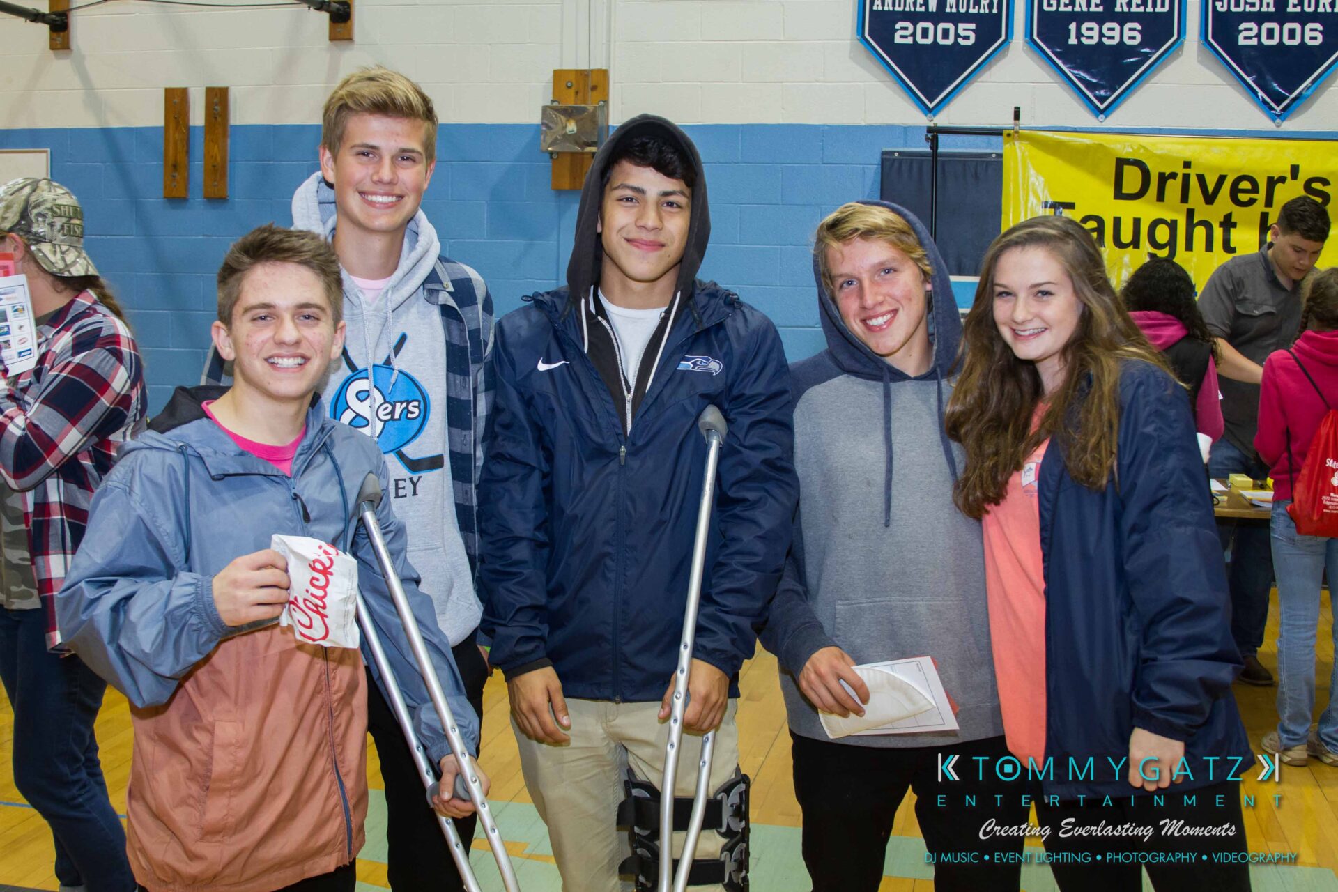 Ford-Driving-Skills-For-Life-20 - TOMMY GATZ ENTERTAINMENT Five young people smiling, one on crutches, standing in a gymnasium with banners and a "Driver's" sign in the background.