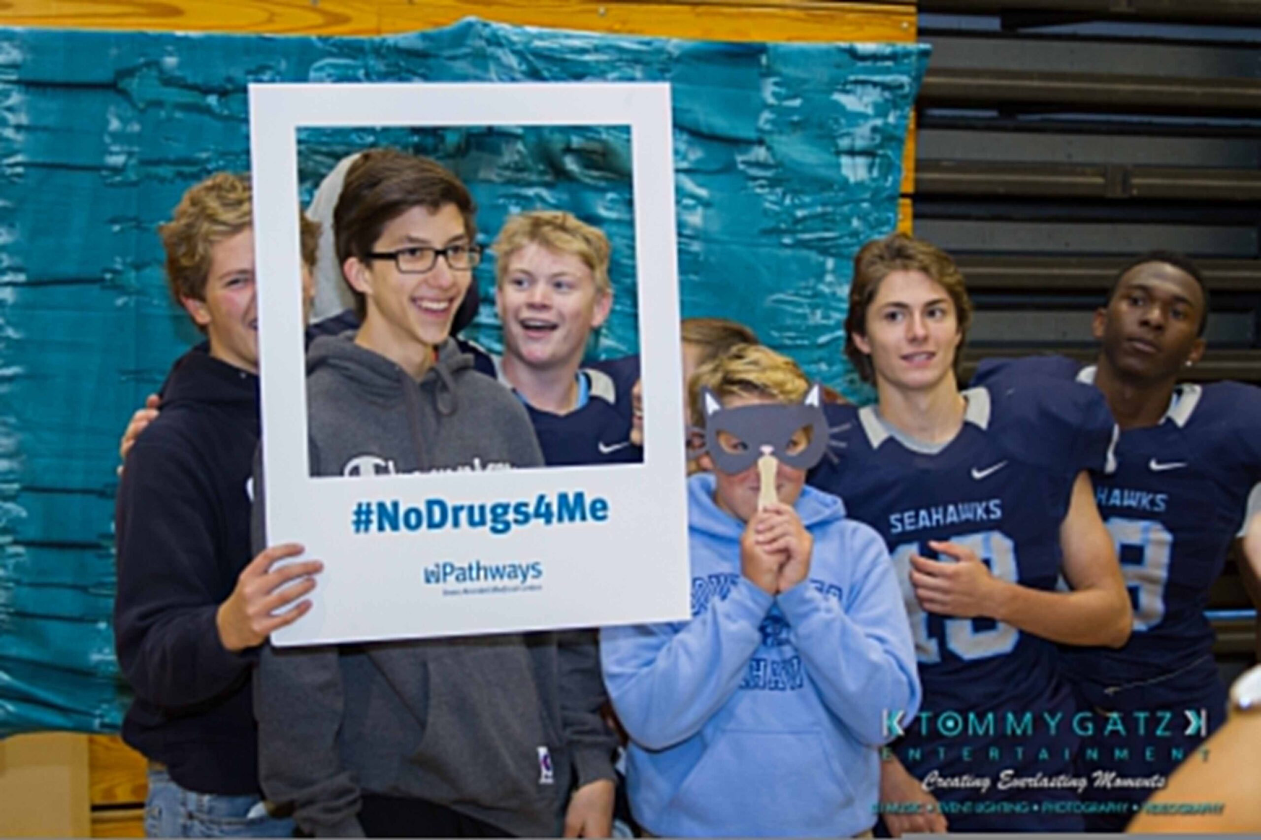 Ford-Driving-Skills-For-Life-24 - TOMMY GATZ ENTERTAINMENT Group of young people, some in sports uniforms, holding a "#NoDrugs4Me" photo frame and mask, standing in front of a painted backdrop in a gymnasium.