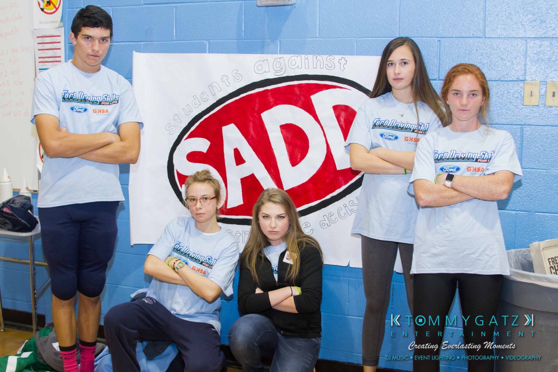 Ford-Driving-Skills-For-Life-42 - TOMMY GATZ ENTERTAINMENT Five students stand together in front of a banner that reads "SADD." They are wearing matching blue shirts and posing with serious expressions.