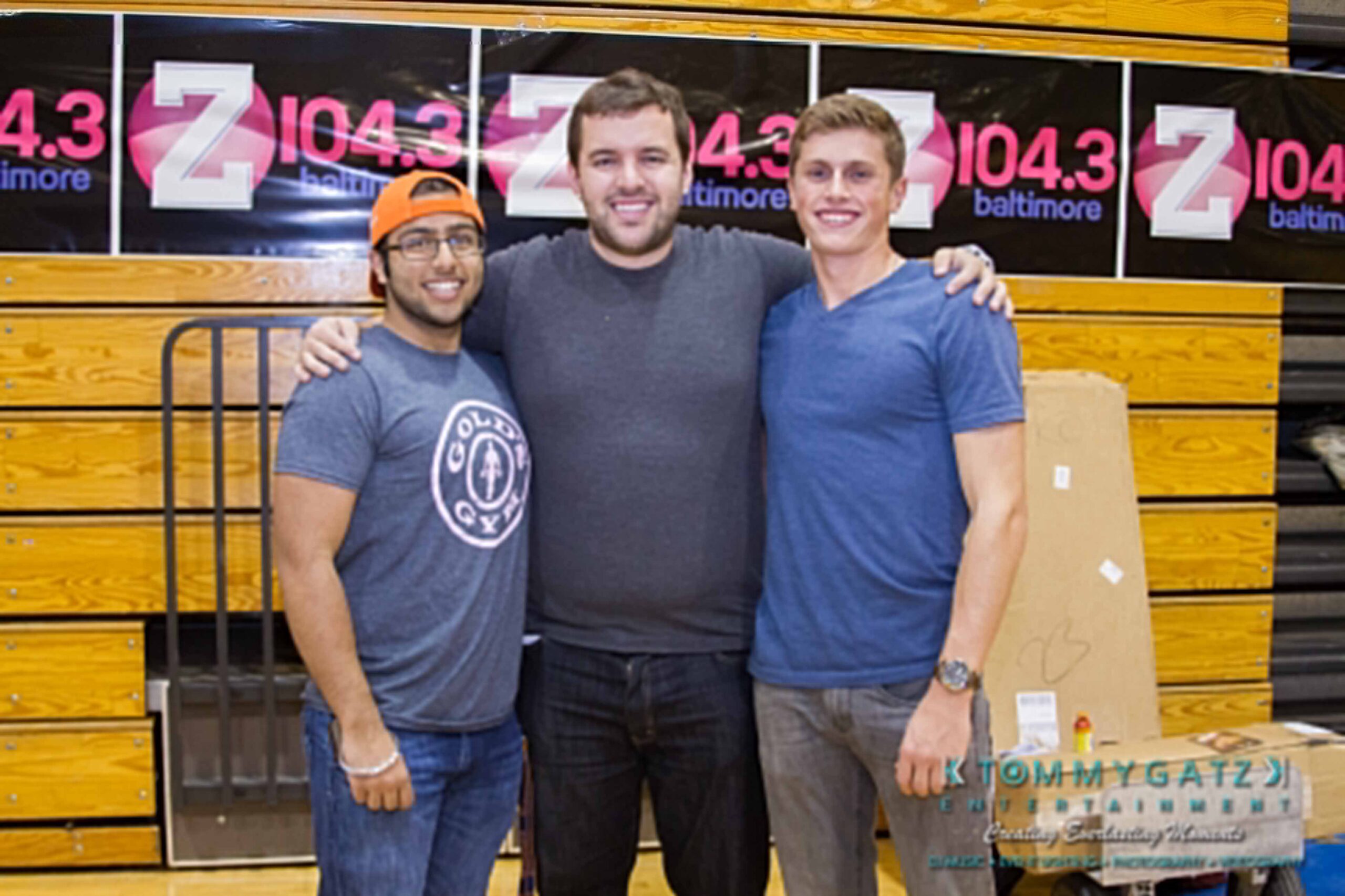 Ford-Driving-Skills-For-Life-51 - TOMMY GATZ ENTERTAINMENT Three men standing together, posing for a photo in front of a gym wall with "Z 104.3 Baltimore" banners.