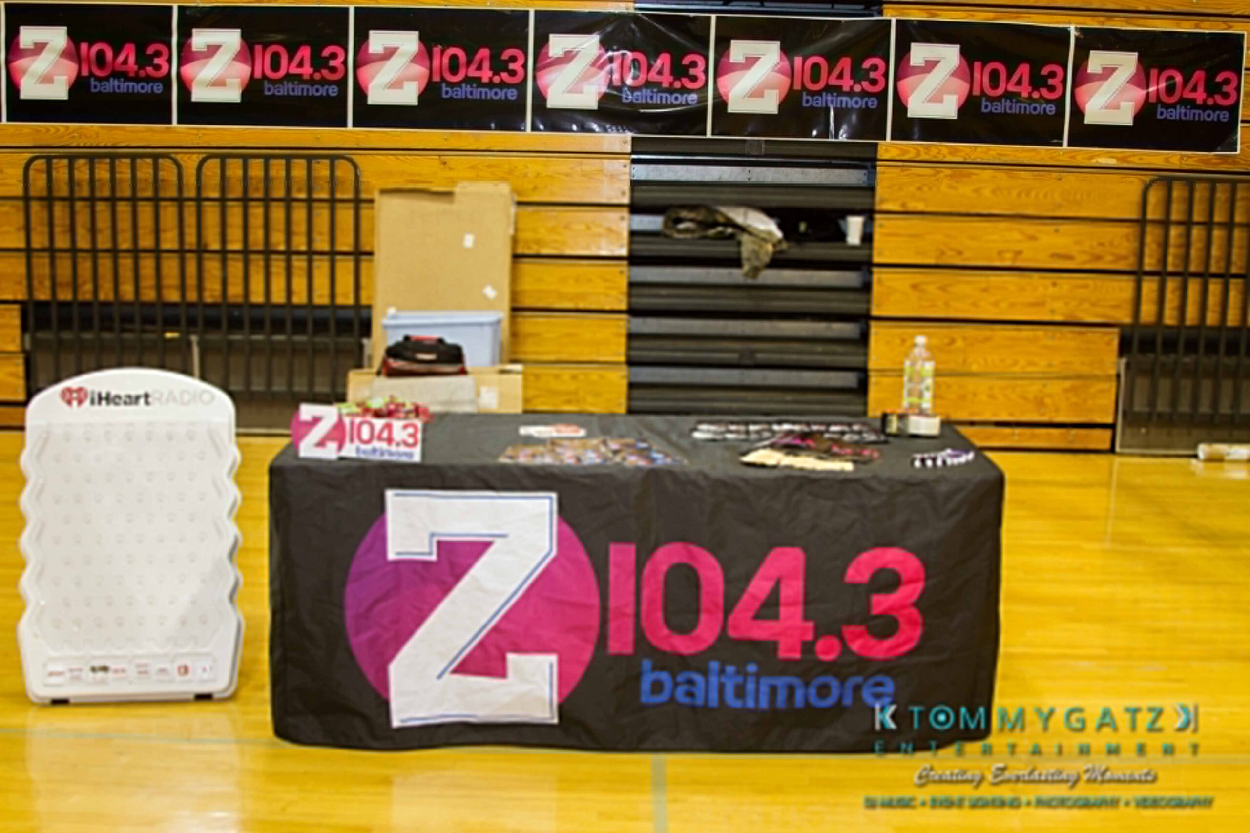 Ford-Driving-Skills-For-Life-54 - TOMMY GATZ ENTERTAINMENT Booth displaying Z104.3 Baltimore branding materials with a table, backdrop, and promotional items in a gymnasium.
