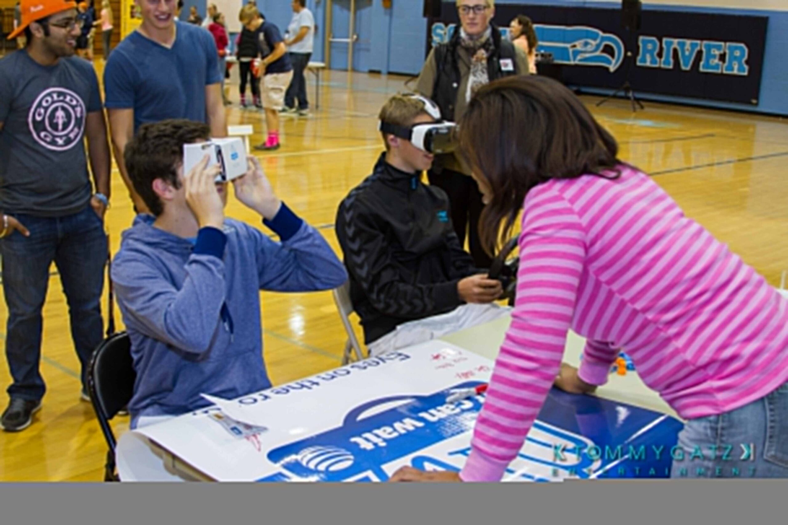 Ford-Driving-Skills-For-Life-8 - TOMMY GATZ ENTERTAINMENT People at a gymnasium event trying virtual reality headsets, with a table displaying a large poster.